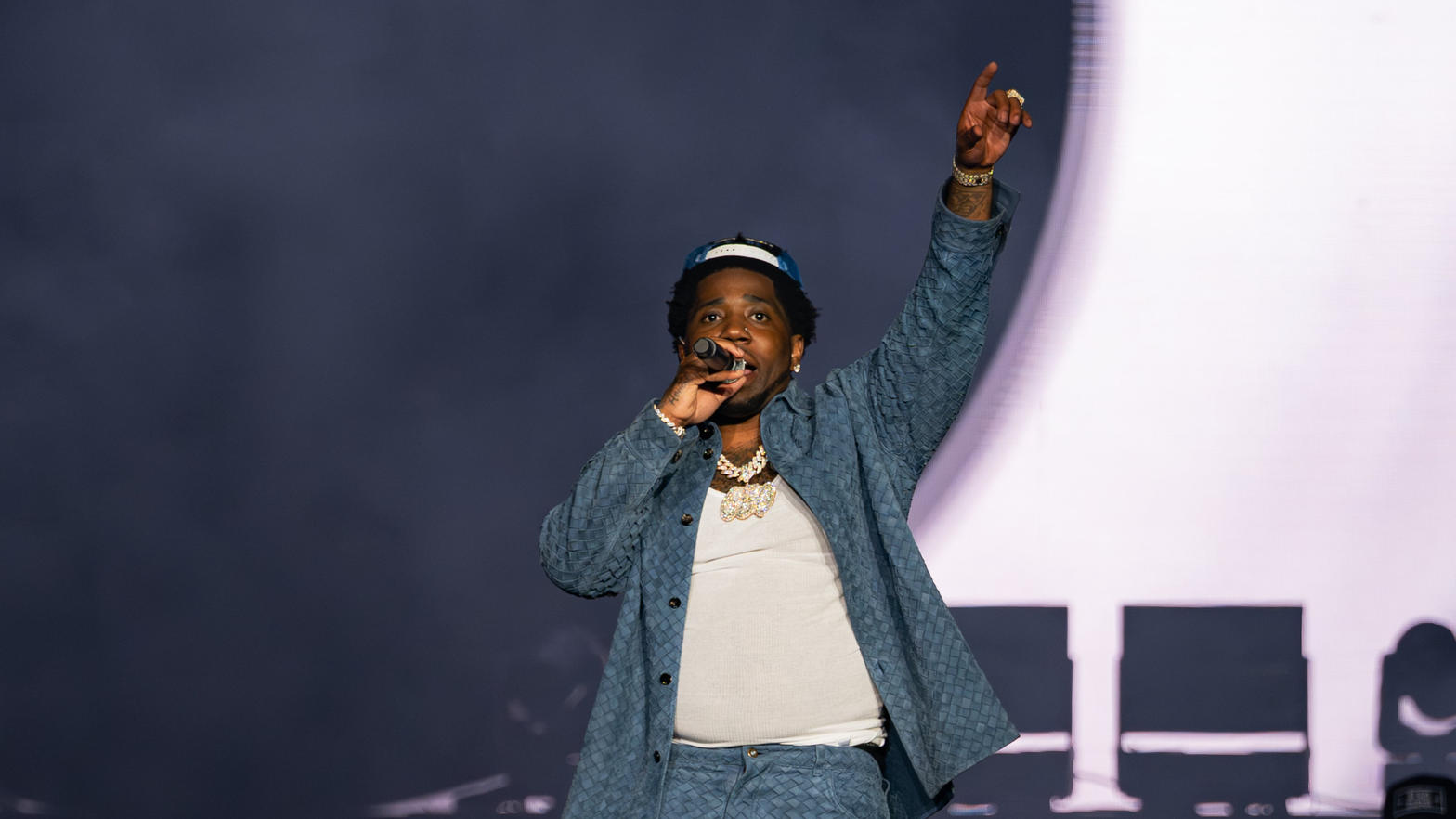 YFN Lucci performing on stage, arm raised under a white spotlight